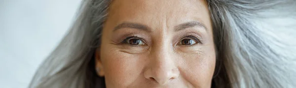Mediana edad mujer asiática con vuelo hoary cabello mira en cámara sobre fondo gris claro — Foto de Stock