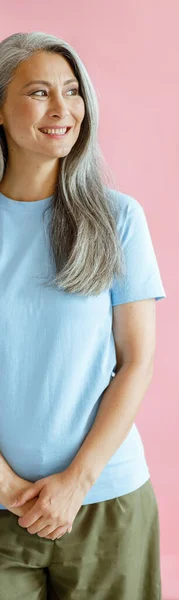 Happy silver haired middle aged aziatische vrouw in t-shirt staat op roze achtergrond — Stockfoto