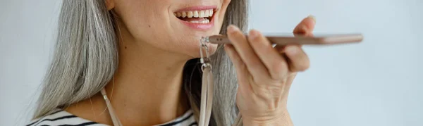 Señora madura positiva con portapapeles utiliza el modo de altavoz en el teléfono sobre fondo gris claro —  Fotos de Stock