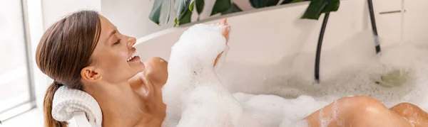 Bathing young woman relaxing in bath, smiling and playing with bubble foam — Stock Photo, Image