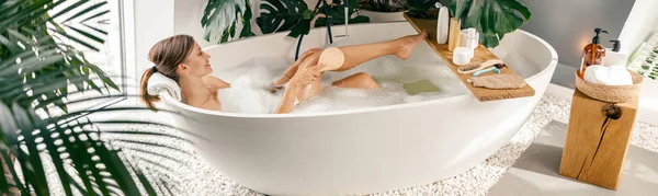 Zrelaksowany młoda kobieta za pomocą szczotki podczas kąpieli bąbelkowej w nowoczesnej łazience urządzone z roślin tropikalnych — Zdjęcie stockowe
