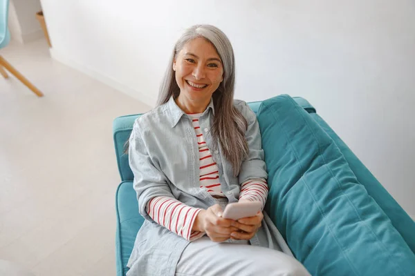 Mujer alegre con teléfono inteligente descansando en el sofá en casa —  Fotos de Stock