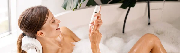 Mujer joven feliz sonriendo mientras toma un baño de burbujas y cuida su piel en un spa de lujo — Foto de Stock