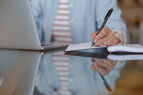 Woman using laptop and writing in notebook at home