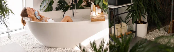 Расслабленная молодая женщина купается в современном интерьере ванной комнаты с тропическими растениями — стоковое фото