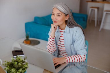 Evde dizüstü bilgisayarda çalışan gülümseyen kadın.