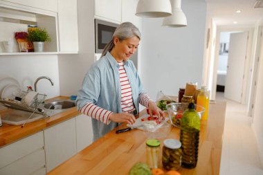 Neşeli kadın mutfakta taze salata yapıyor.