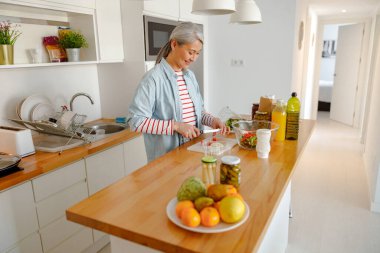 Gülümseyen kadın mutfakta salata malzemeleri hazırlıyor.