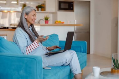 Kanepede oturan ve evde not defteri kullanan neşeli bir kadın.