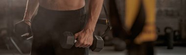 Spor salonunda iki dambılı tutan beden eğitimi hocası.