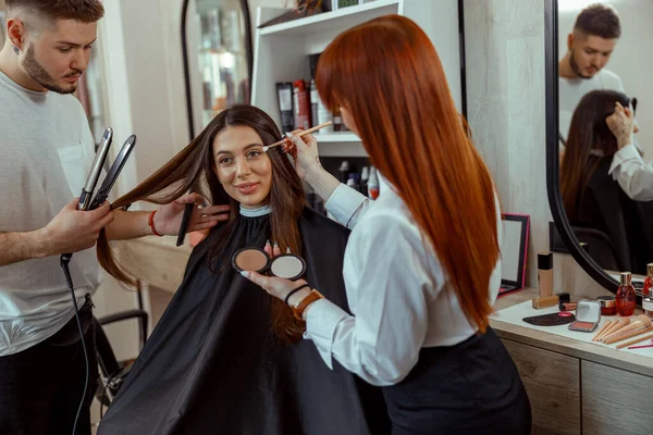 Artista de maquillaje profesional y estilista preparando cliente femenino en salón de belleza —  Fotos de Stock