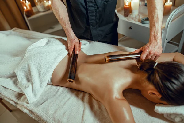 Male therapist hands doing back massage to female client with hollow bamboo canes — Stock Photo, Image