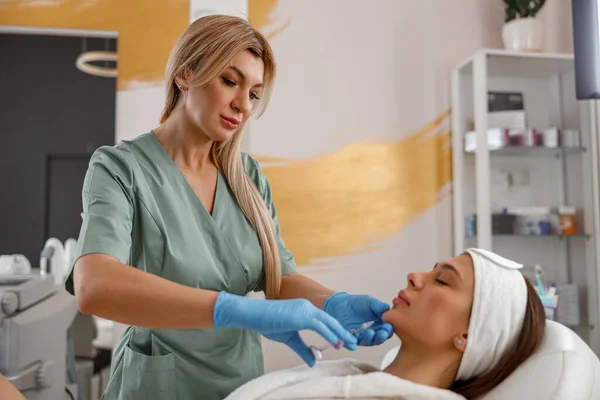 Expert beautician filling female chin with hyaluronic acid in beauty salon
