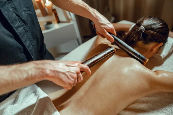 Primo piano di mani terapeuta maschile facendo massaggio alla schiena alla donna utilizzando canne di bambù cavo — Foto Stock