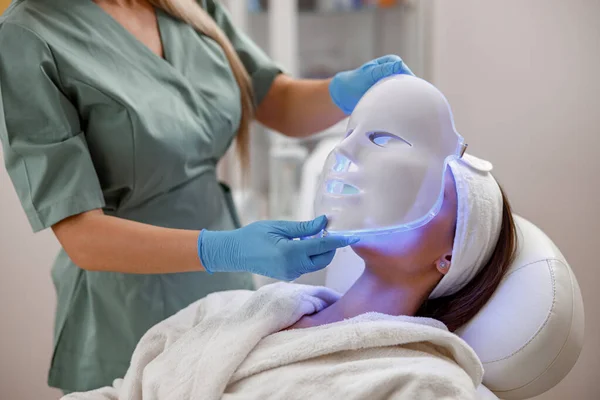 Cosmetic procedure with LED facial mask for female face. Photon therapy