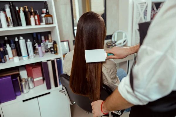 Cabeleireiro escovação longo e elegante cabelo castanho do cliente feminino no salão de beleza — Fotografia de Stock