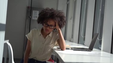 Modern minimalist ofisteki yorgun genç iş kadını kafasını tutuyor ve mutsuz oturuyor.