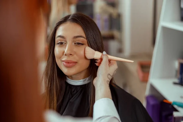 Nahaufnahme des Gesichts einer jungen Frau, die mit einem Pinsel Puder auf ihre Wange bekommt — Stockfoto