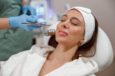 Kozmetik uzmanı yüzünü süpürgeyle temizliyor. Kaplıcada gençleştirme ve su kaybı