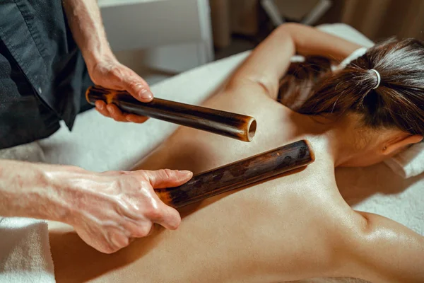 Primo piano mani maschili facendo massaggio alla schiena alla donna utilizzando canne di bambù cave — Foto Stock