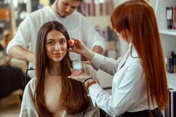 Kadın kameraya bakıyor, kuaförde profesyonel makyaj ve saç stili yaptırıyor.