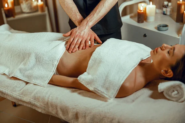 Erkek terapist, spa salonunda parmaklarıyla karın masajı yapıyor.