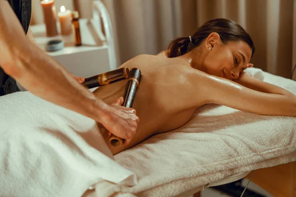 Чоловічий терапевт робить масаж спини та плечей для жінки, використовуючи пустотілі бамбукові палички — стокове фото