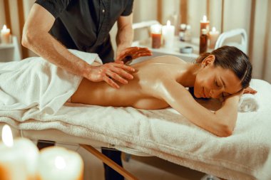 Erkek masör, spa salonunda içi boş bambu bastonları olan bir kadın için sırt masajı yapıyor.