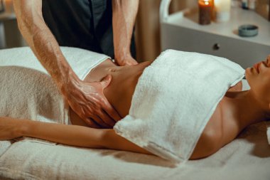 Rahatlamış genç bir kadın spa salonunda profesyonel mide masajı yaptırıyor.