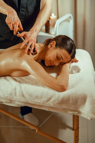 Happy female client getting back massage with hollow bamboo holes at spa salon — Stock fotografie