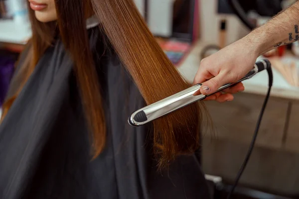 Närbild av frisör hand hålla hår plattång och göra frisyr för kvinnlig klient — Stockfoto