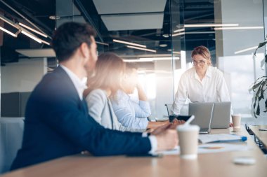 Resmi giyinmiş bir grup meslektaşım masada iş görüşlerini tartışıyor ve birlikte çalışıyorlar.