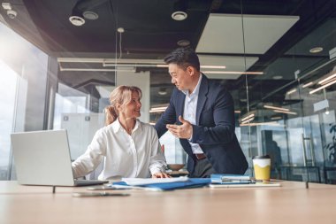 Ofisteki toplantı masasında dizüstü bilgisayarla çalışırken gülümseyen iki farklı iş adamı.