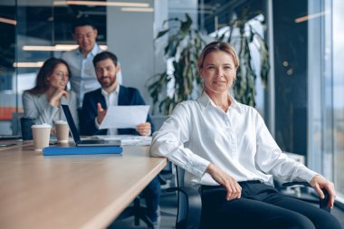 Ofiste iş arkadaşlarıyla otururken gülümseyen kendine güvenen bayan patron. 