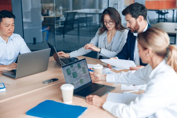 Odaklanmış iş adamları ofiste konferans sırasında cihazlar kullanıyor ve konuşuyorlar.