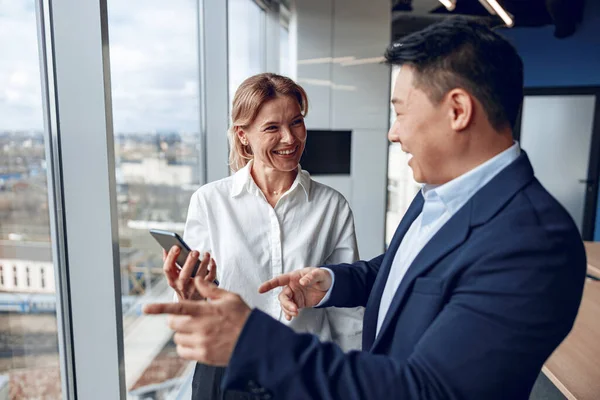 Confident asian businessmen talks to his mature female partner while standing near panoramic window — Stock Photo, Image