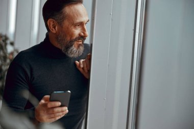 Pencereden dışarı bakan telefonla gülümseyen bir adam.