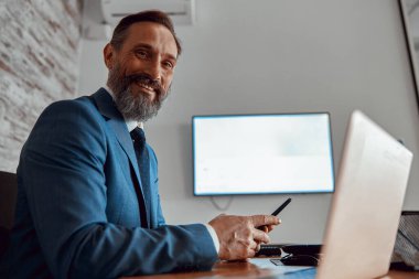 Takım elbiseli şık bir adam cep telefonunu odada tutuyor.