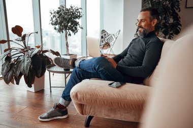 Koltukta oturup dizüstü bilgisayar kullanan neşeli bir adam.