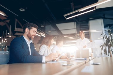 Yaratıcı gülümseyen iş adamı bir ekiple yaptığı toplantıda tablet üzerinde çalışıyor.