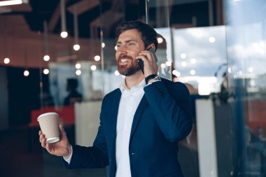 Kahve fincanı alıp müşterisiyle konuşan yakışıklı bir ofis çalışanı.