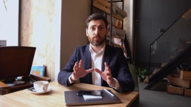 Cheerful businessman vlogger telling something to camera in cafe and explaining. Business coach.