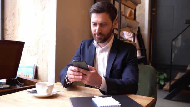 Handsome Caucasian man in suite texting message on smartphone in cafe. Businessman chatting. — Vídeos de Stock