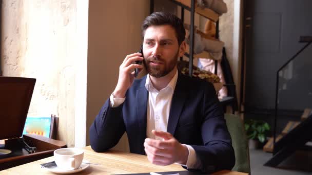 Handsome man in elegant style having talk on cellphone, sitting in cafe. Coffee break conversation. — Vídeos de Stock