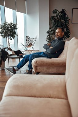 Yetişkin bir adam dairesinde dinleniyor ve koltuğunda oturuyor.