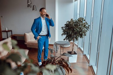 Pencerenin önünde duran bir adam telefonla konuşmaktan zevk alıyor.