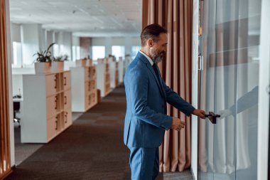 Smiling businessman in a suit entering the glass door