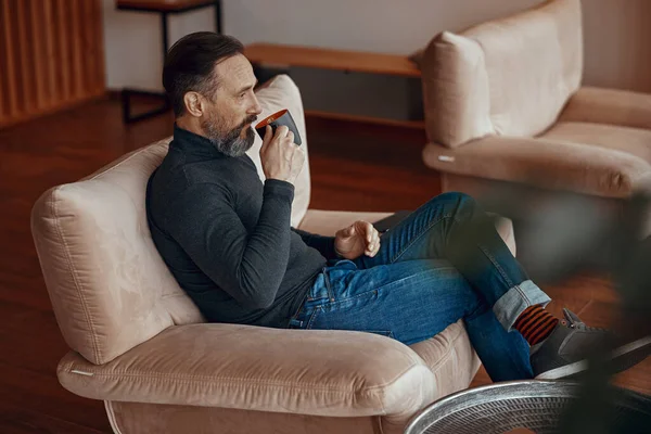 Handsome man enjoying coffee while relaxing in armchair — Stock Photo, Image