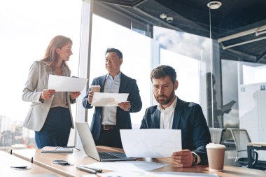 Gülümseyen işadamları toplantı sırasında modern bir ofiste grafik ve çizelgelerle belgeleri tartışıyorlar.