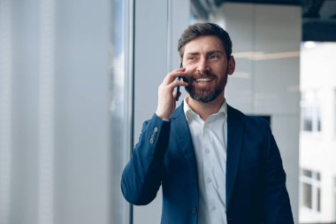 Smiling businessman uses mobile phone to call his business partner while working in the office